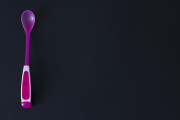 Fototapeta na wymiar pink baby spoon on a black background