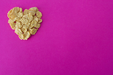 Corn flakes in the form of heart on a pink background