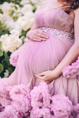 pregnant woman is standing in a pink dress with ruffles in the garden