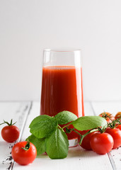 Tomato juice in a glass with a cherry and basil on a light background