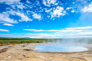A wide angle view from the hills of geysir in Iceland, with a clear blue hot spring in foreground