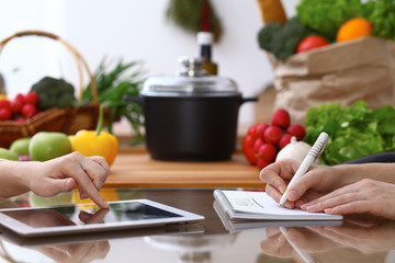 Closeup of human hands cooking in kitchen. Women discuss a menu using tablet computer. Copy space area at touch pad. Healthy meal, vegetarian food and lifestyle concepts