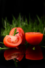 Tomato isolated on the black and glossy background with realistic reflection and water drops