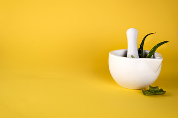 Aloe vera leaf, white mortar full of chopped aloe and bottles of aloe gel or infusion.