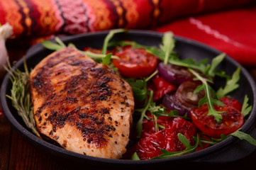 Grilled chicken breast with green salad from arugula and vegetables on a black pan. Wooden rustic background. Top view