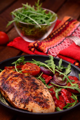 Grilled chicken breast with green salad from arugula and vegetables on a black pan. Wooden rustic background. Top view