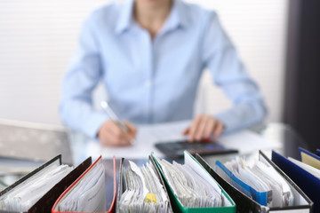Binders with papers are waiting to be processed with businesswoman or secretary back in blur