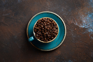 Natural organic roasted coffee beans in blue cup on dark rusty background, top view, flat lay, copy space.