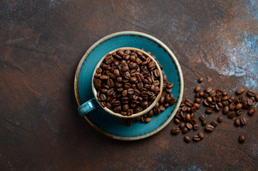 Natural organic roasted coffee beans in blue cup on dark rusty background, top view, flat lay, copy space.