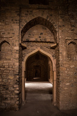 Mandu India, afghan ruins of islam kingdom, palace interior, mosque monument and muslim tomb. Sunshine from door in dark corridor.