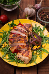 Grilled chicken breast with green salad from arugula and vegetables on a yellow plate. Wooden rustic background. Top view