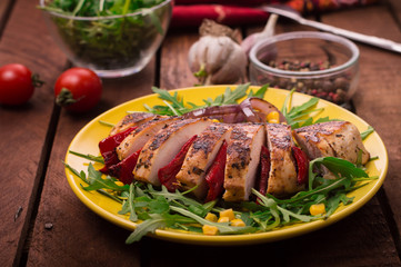 Grilled chicken breast with green salad from arugula and vegetables on a yellow plate. Wooden rustic background. Top view