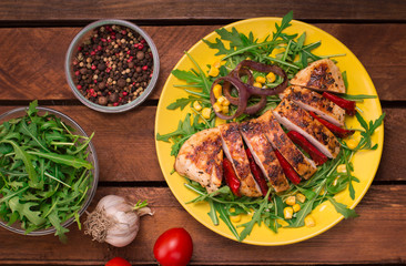Grilled chicken breast with green salad from arugula and vegetables on a yellow plate. Wooden rustic background. Top view
