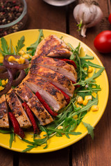 Grilled chicken breast with green salad from arugula and vegetables on a yellow plate. Wooden rustic background. Top view