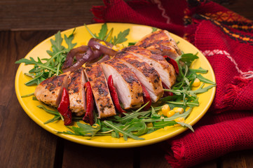 Grilled chicken breast with green salad from arugula and vegetables on a yellow plate. Wooden rustic background. Top view