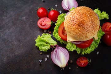 Beef burgers with vegetables. Lies on black textured background with lettuce, tomatoes and spices....