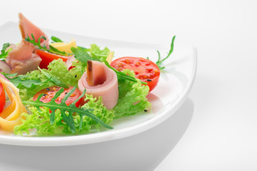 Fresh salad with tomatoes, arugula, cheese and ham on the white plate and white background