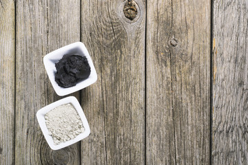 gray cosmetic clay powder and black mud on old wood texture