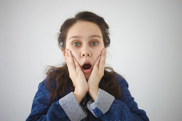 Human emotions, feelings, reaction and attitude. Horizontal shot of amazed female teenager opening mouth widely and holding her cheeks, expressing shock and full disbelief, posing isolated in studio