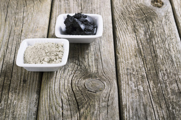 gray cosmetic clay powder and black mud on old wood texture