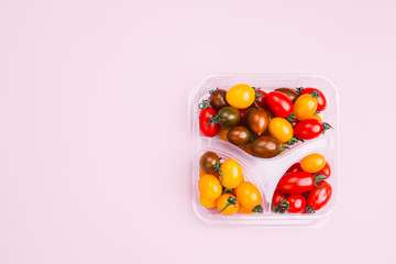 Freshly colored mixed  cherry tomatoes
inside a market plastic container  ,top view, over a Pink background
