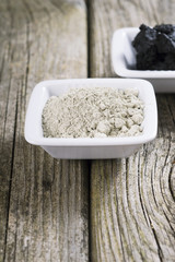 gray cosmetic clay powder and black mud on old wood texture
