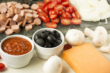 Ingredients for Italian pizza with cheddar cheese, mushrooms, black olives and sausage on white wooden background 