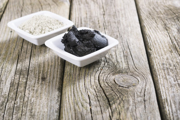 gray cosmetic clay powder and black mud on old wood texture