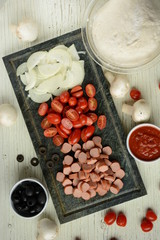 Ingredients for Italian pizza with cheddar cheese, mushrooms, black olives and sausage on white wooden background 