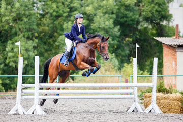 Young girl riding sorrel horse on show jumping competition