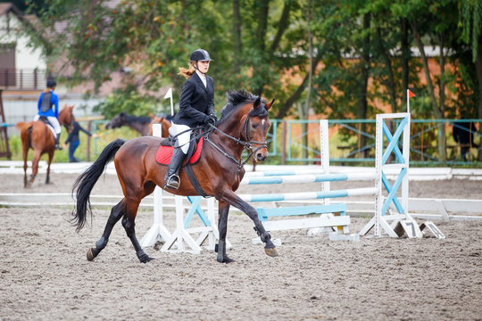 Young girl riding bay horse on show jumping competition