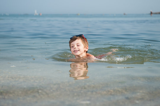 happy smiling cute little boy in sunglasses swimming in sea water in summer sunny day holiday enjoying