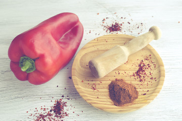 Red pepper with paprika on wooden plate on white wooden background