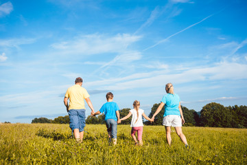 Family holding hands running over meadow, mother, father and children