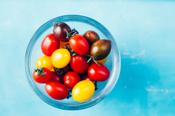 Freshly colored mixed  cherry tomatoes
inside a jar ,top view, over a blue background