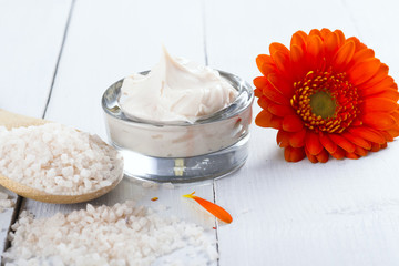 sea clay powder, moisturizer and bath salt with gerbera flower on white wooden table background