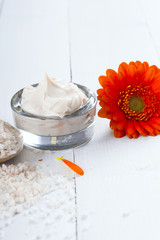sea clay powder, moisturizer and bath salt with gerbera flower on white wooden table background