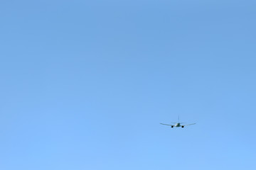 The passenger plane flies away into the blue sky. Back view