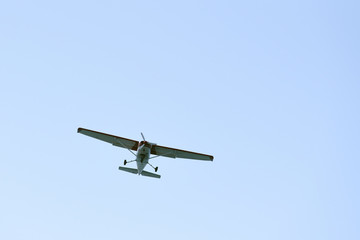 Fototapeta na wymiar The light airplane flies low overhead on a blue sky background. Bottom view