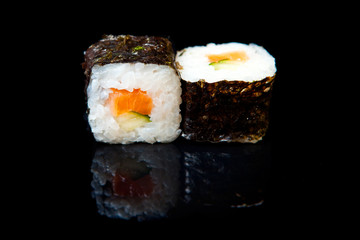 Traditional fresh japanese sushi rolls on a black background with reflection.