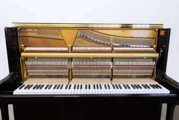 Internal parts of a black upright piano - keyboard, mechanics and strings, front view