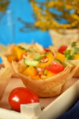 Vegetable salad served in filo tartlets on blue background
