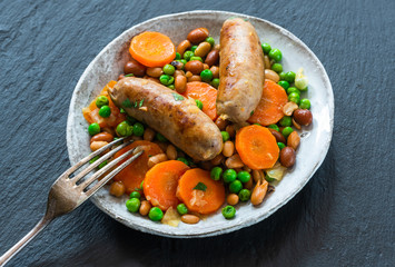 Sausage and bean casserole with carrots and green peas - top view