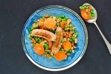 Sausage and bean casserole with carrots and green peas - top view