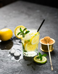 Lemon fruit lime slices caipirinha from Brazil, lemonade mint ice cubes in cold glasses on dark background, alcoholic mojito cockail ice tea green mint leaves, brown sugar spoon, copy space