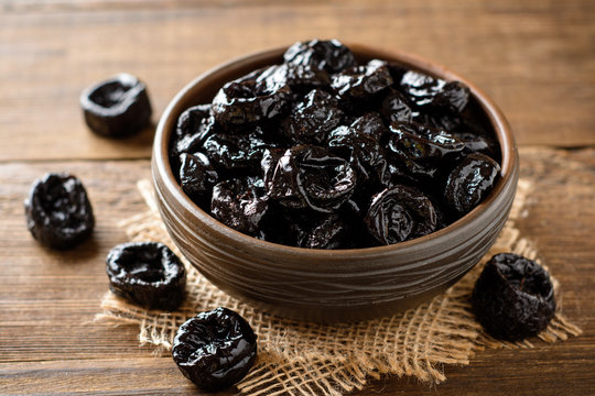 Prunes in ceramic bowl on rustic wooden table. Dried plums.
