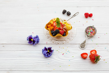 Naklejka na ściany i meble Ice cream in waffle basket with edible flowers *pansy, violet on white old wooden rustic background. Pink (strawberry), yellow (mango or banana) and green (lime, green tea or pistachio). Top view
