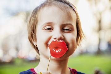 Cute little child girl holding fake paper smile in front of lips.