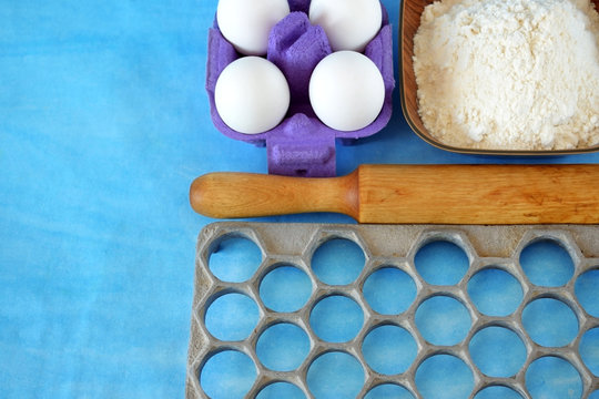 Eggs, flour and kitchen utensils for cooking homemade dumplings on blue background