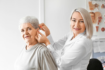 Otolaryngologist putting hearing aid in senior woman's ear in hospital